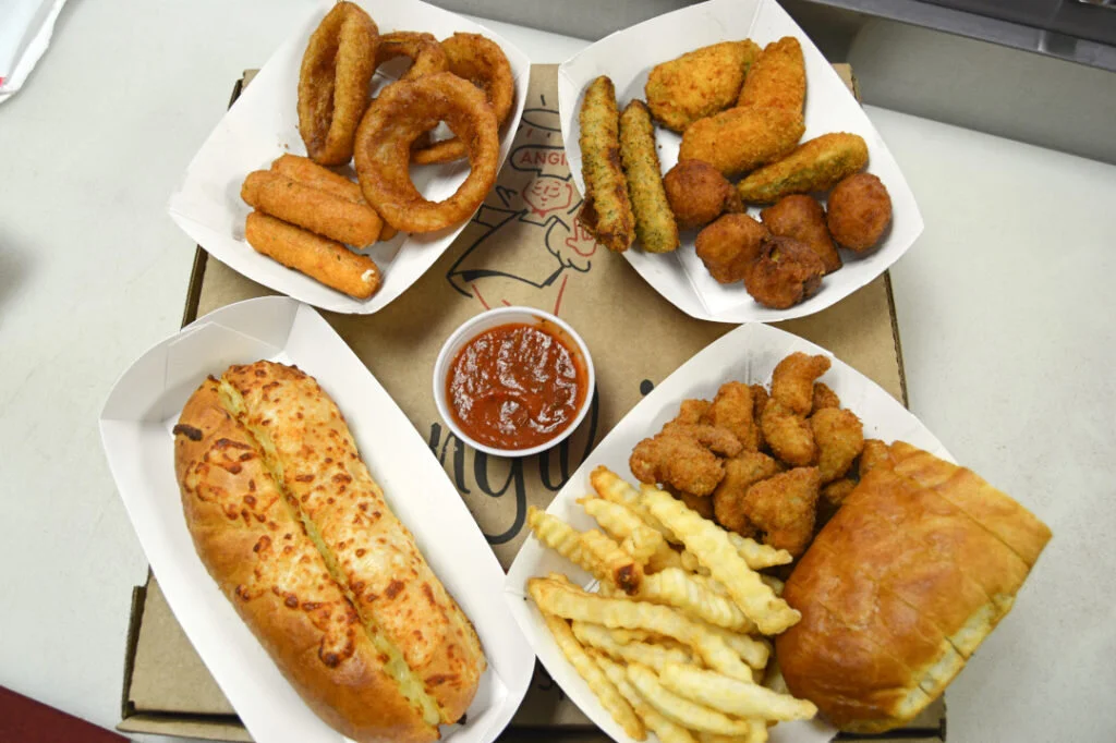 An appetizer spread on an Angilo's pizza box: onion rings, mozzarella sticks, fried pickles, mushrooms, cheese breadsticks, fries and marinara.
