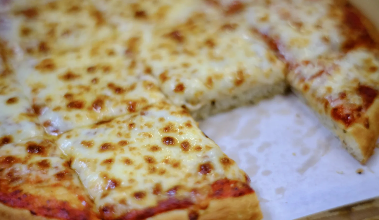 Close-up of a fresh cheese pizza with browned, bubbling mozzarella, one slice pulled away.