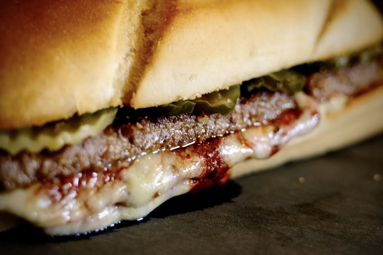 A hot stromboli on a hoagie bun, layered with melted cheese, sauce and pickles.
